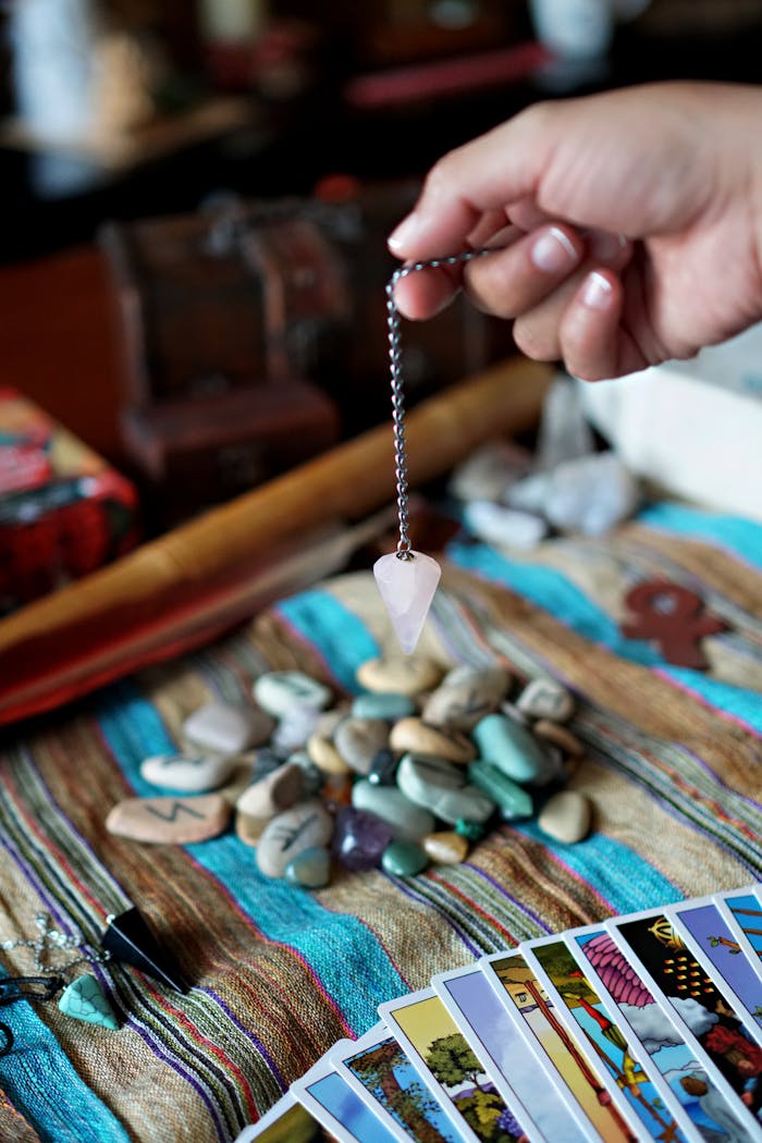 Mastering the First Impression: Your intriguing post title goes here A hand holds a pendulum over a collection of tarot cards and stones, suggesting a mystical or spiritual setting.